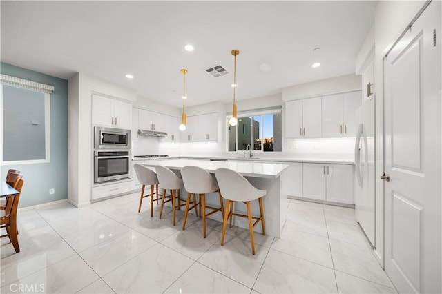 kitchen featuring a breakfast bar area, under cabinet range hood, stainless steel appliances, a sink, and visible vents