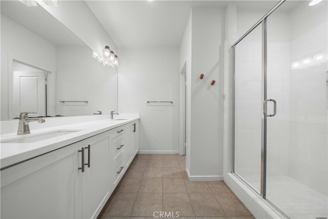 bathroom featuring double vanity, a sink, a shower stall, baseboards, and tile patterned floors