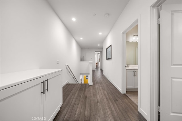 corridor featuring baseboards, dark wood-style floors, an upstairs landing, a sink, and recessed lighting