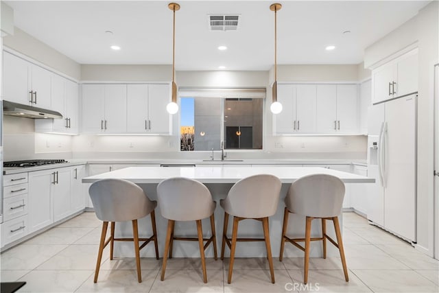 kitchen with under cabinet range hood, white refrigerator with ice dispenser, gas stovetop, a sink, and visible vents