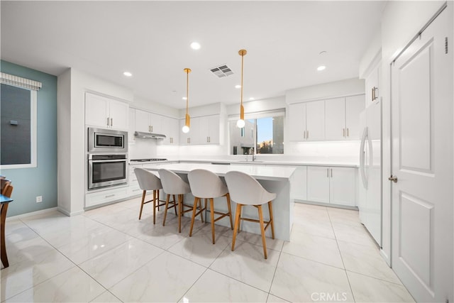 kitchen with a breakfast bar, stainless steel appliances, light countertops, visible vents, and a kitchen island