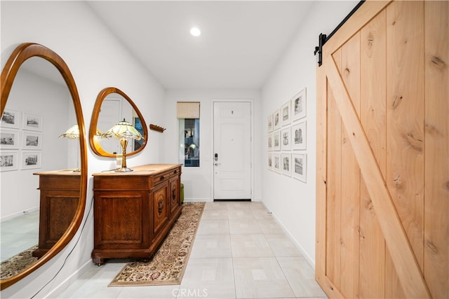 entryway with light tile patterned floors, a barn door, and baseboards