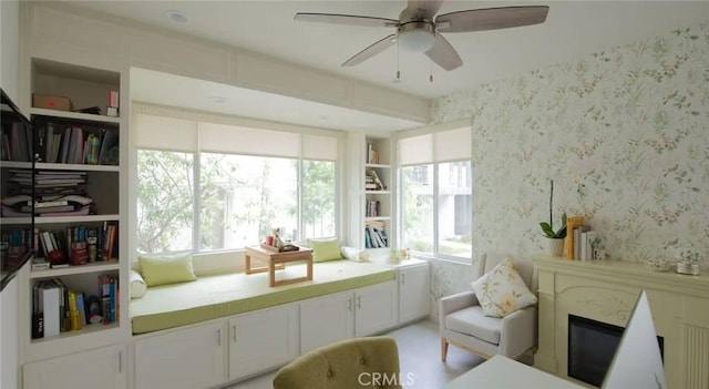 living area with wallpapered walls, ceiling fan, and a glass covered fireplace