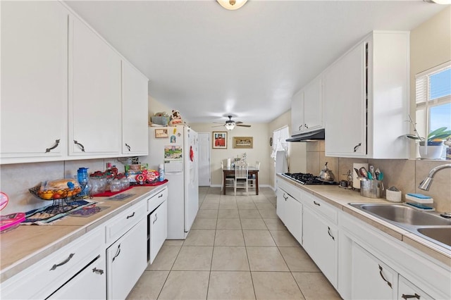 kitchen with white refrigerator with ice dispenser, backsplash, light countertops, under cabinet range hood, and a sink