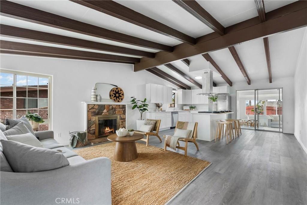 living area with a stone fireplace, lofted ceiling with beams, and light wood-style flooring