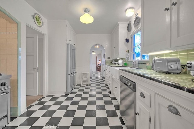 kitchen featuring arched walkways, stainless steel appliances, tile counters, white cabinetry, and dark floors