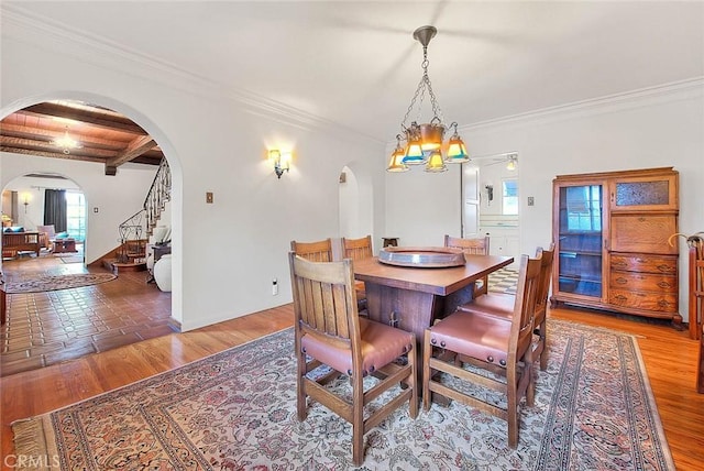 dining space featuring beamed ceiling, ornamental molding, stairway, arched walkways, and light wood finished floors