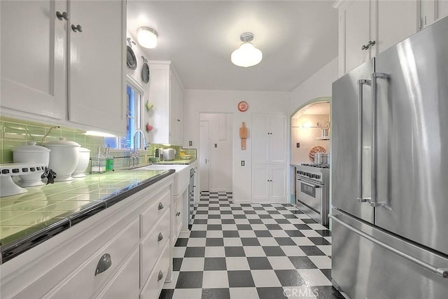 kitchen featuring tile countertops, high end appliances, a sink, white cabinetry, and dark floors