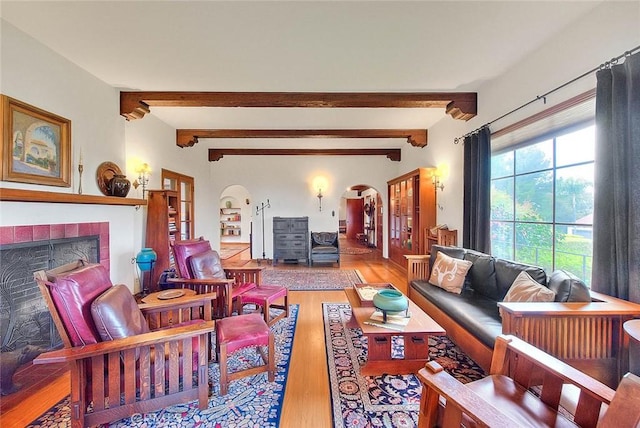 living room with arched walkways, beam ceiling, a fireplace, and wood finished floors