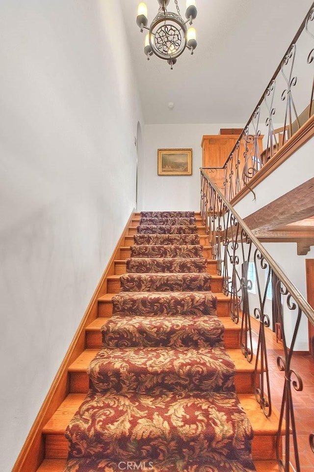 staircase featuring baseboards, a notable chandelier, a high ceiling, and arched walkways