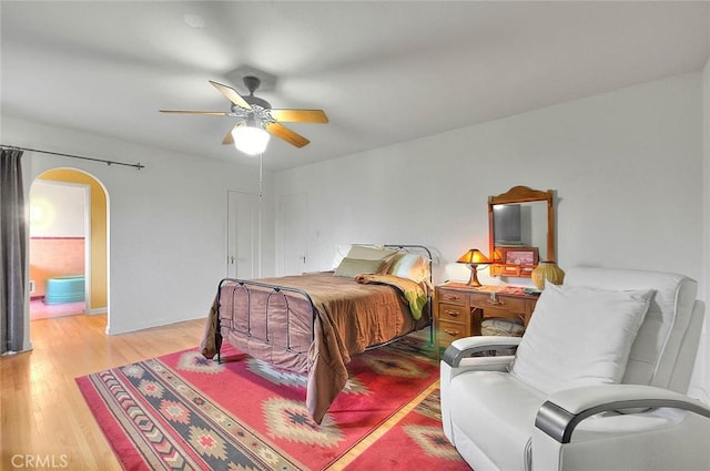 bedroom with arched walkways, wood finished floors, and a ceiling fan