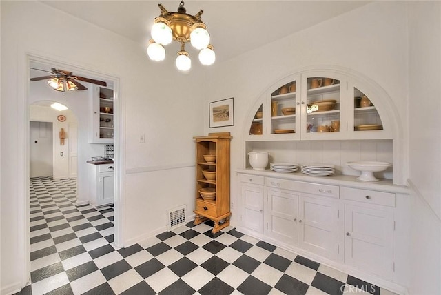 unfurnished dining area with visible vents, arched walkways, light floors, and ceiling fan with notable chandelier