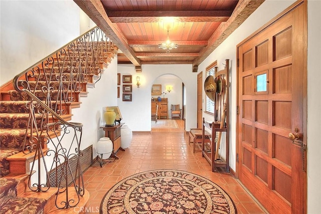 foyer entrance with arched walkways, beam ceiling, wooden ceiling, and stairway