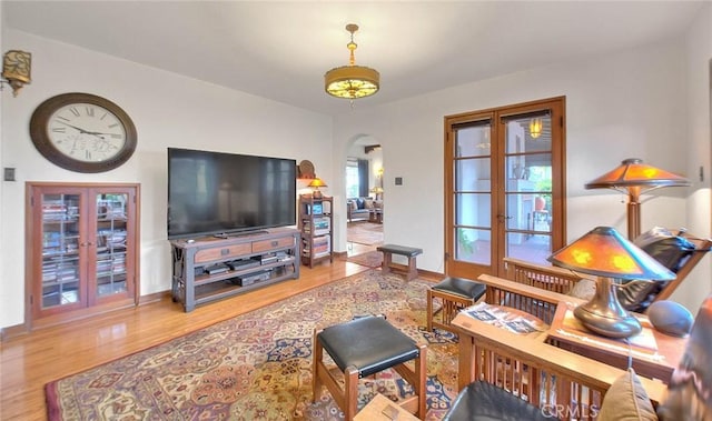 living area featuring arched walkways, french doors, baseboards, and wood finished floors