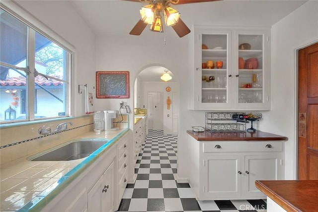 kitchen featuring arched walkways, a sink, glass insert cabinets, white cabinetry, and tile patterned floors