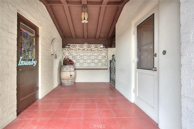 corridor featuring beam ceiling, dark tile patterned floors, wooden ceiling, and brick wall