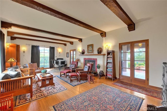 living room featuring beam ceiling, a brick fireplace, wood finished floors, and french doors