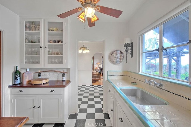 kitchen featuring arched walkways, a sink, glass insert cabinets, white cabinetry, and tile patterned floors