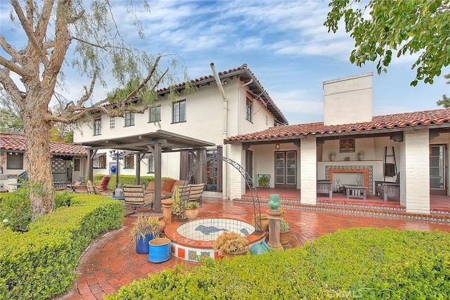 back of house with a tile roof, stucco siding, a chimney, and a patio