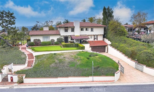 mediterranean / spanish home featuring a tiled roof, a front yard, stucco siding, a chimney, and driveway