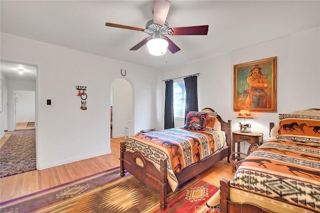 bedroom with baseboards, a ceiling fan, arched walkways, and light wood-type flooring