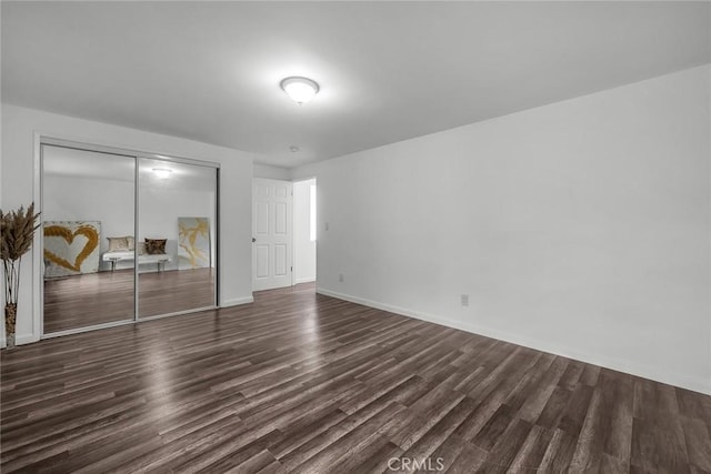 unfurnished bedroom featuring a closet, dark wood-type flooring, and baseboards