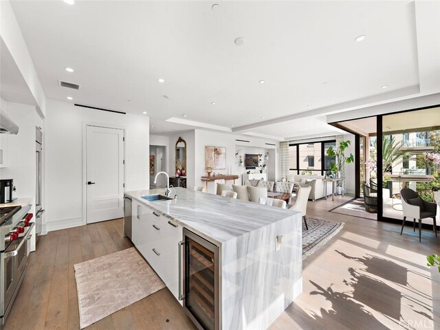 kitchen with a large island, light wood-style floors, white cabinets, a sink, and beverage cooler