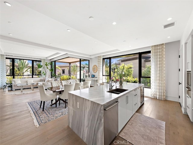 kitchen with visible vents, a large island, modern cabinets, stainless steel dishwasher, and a sink