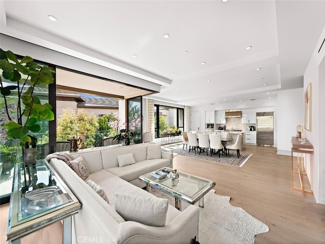 living room with light wood finished floors, a raised ceiling, and recessed lighting