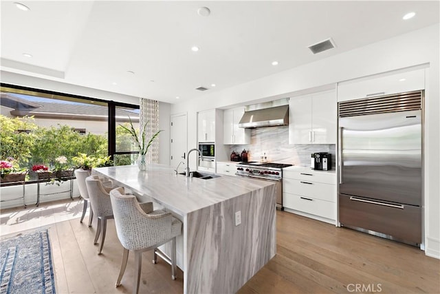 kitchen with premium appliances, wall chimney exhaust hood, modern cabinets, white cabinetry, and a sink