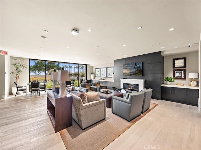 living area featuring expansive windows, light wood finished floors, a glass covered fireplace, and recessed lighting