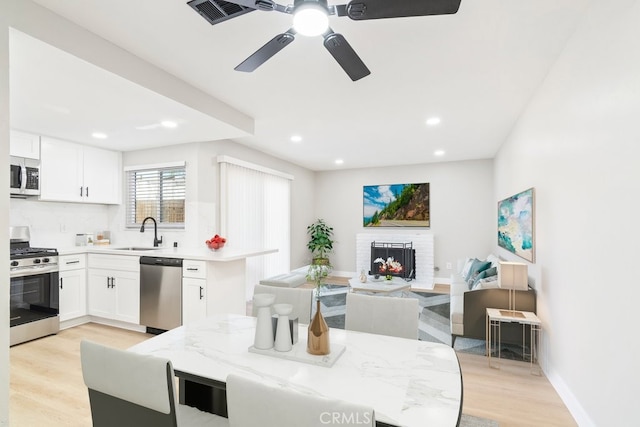 kitchen with appliances with stainless steel finishes, light wood-style floors, a brick fireplace, open floor plan, and a sink