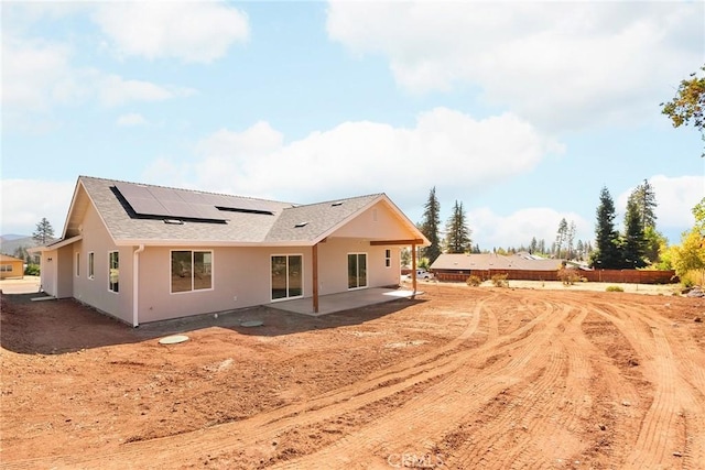 rear view of house with roof mounted solar panels, a patio, and stucco siding