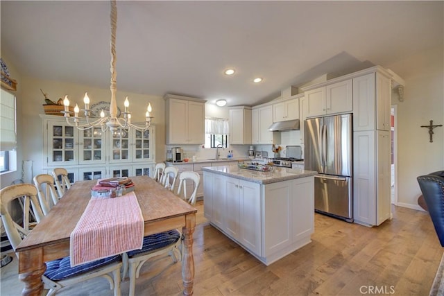 kitchen with under cabinet range hood, a chandelier, white cabinets, stainless steel fridge, and a sink