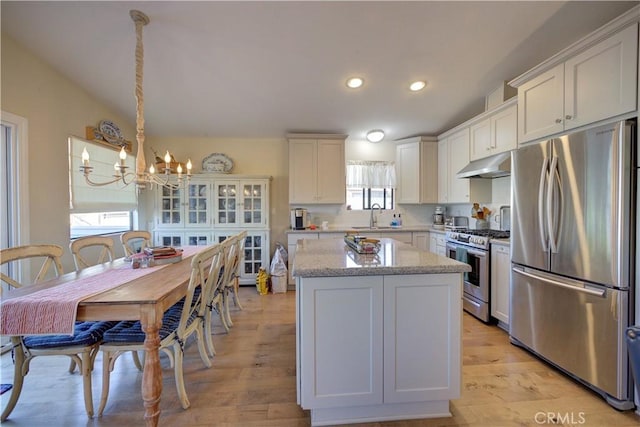 kitchen featuring a center island, under cabinet range hood, stainless steel appliances, white cabinetry, and a sink