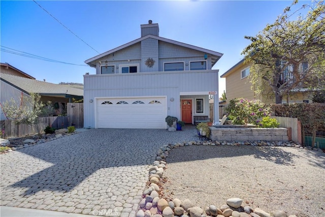 traditional home with decorative driveway, fence, an attached garage, and a chimney