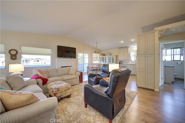 living area featuring a fireplace, lofted ceiling, a healthy amount of sunlight, and light wood finished floors