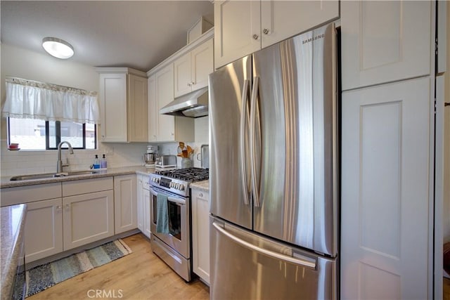 kitchen with a sink, stainless steel appliances, light wood-style floors, under cabinet range hood, and white cabinetry