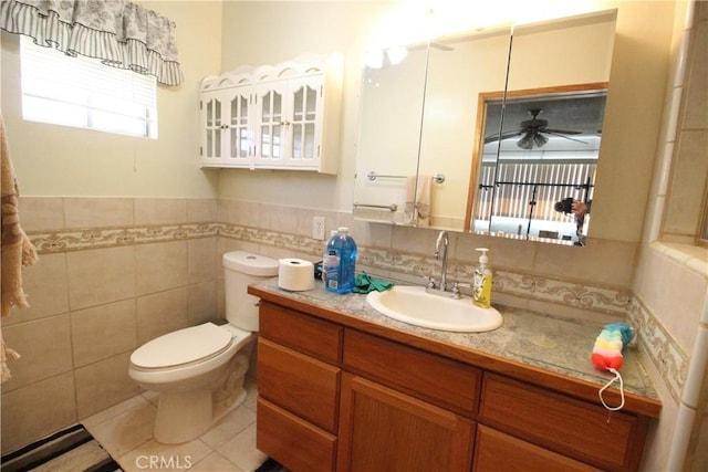 bathroom with a ceiling fan, toilet, a wainscoted wall, vanity, and tile walls