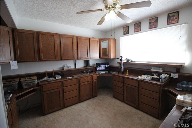 kitchen with brown cabinets, dark countertops, glass insert cabinets, ceiling fan, and a textured ceiling