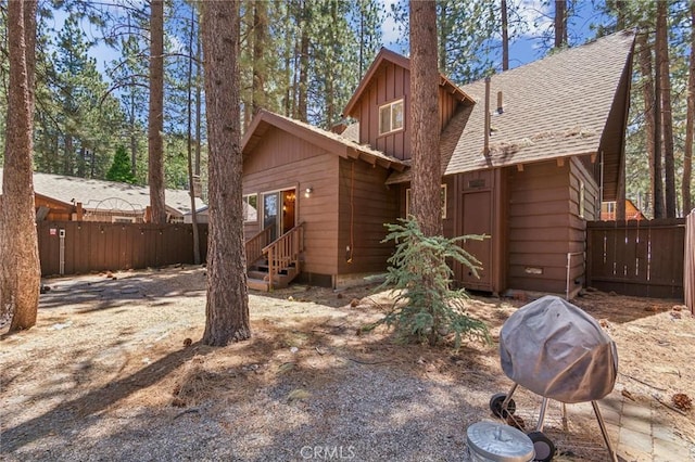 back of house featuring entry steps, fence, board and batten siding, and roof with shingles