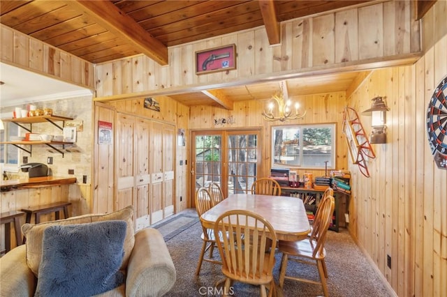 carpeted dining space featuring wood ceiling, beamed ceiling, wood walls, and an inviting chandelier