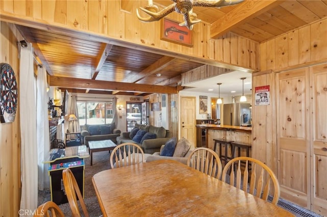 dining area with beam ceiling, wood walls, wood ceiling, and a ceiling fan