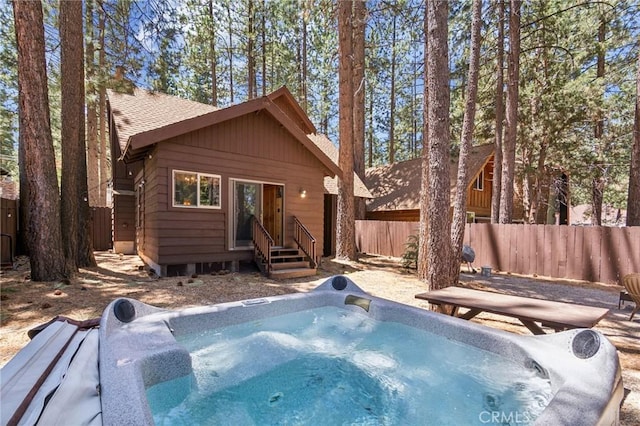 back of house featuring entry steps, a hot tub, fence, and a shingled roof