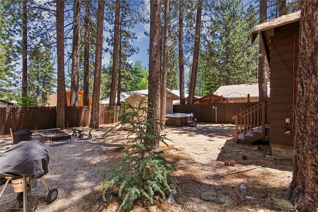 view of yard with a hot tub, an outdoor fire pit, a fenced backyard, and an outbuilding