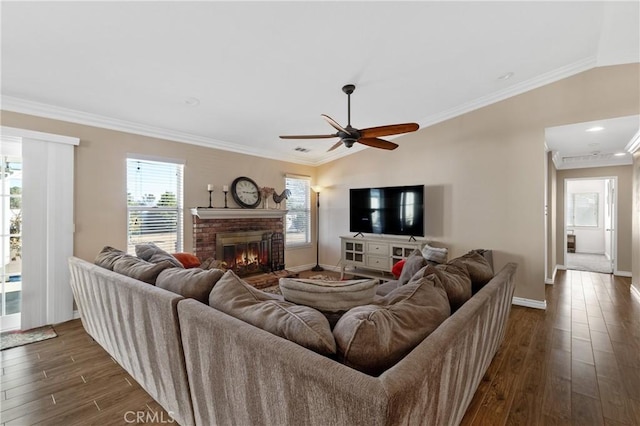 living area with crown molding, baseboards, ceiling fan, a fireplace, and dark wood-style floors