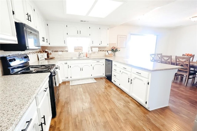 kitchen with a sink, a peninsula, black appliances, and light wood finished floors