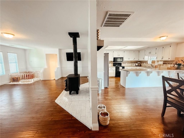 kitchen featuring a breakfast bar, visible vents, a wood stove, a peninsula, and black appliances