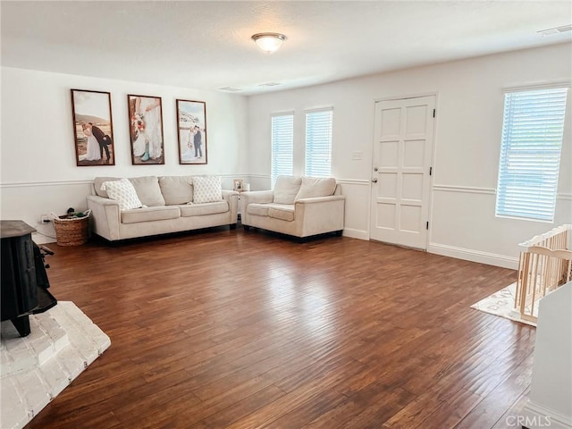 living area with a wood stove, dark wood-style floors, plenty of natural light, and visible vents