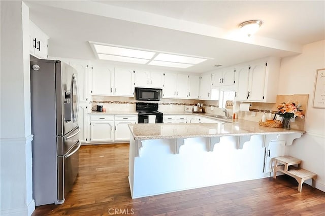 kitchen with black appliances, a peninsula, wood finished floors, and decorative backsplash